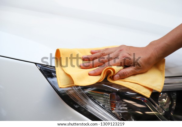 Closeup of\
headlight of white car cleaning, polishing by woman owner\'s hand\
with yellow microfiber cloth in sunny\
day.