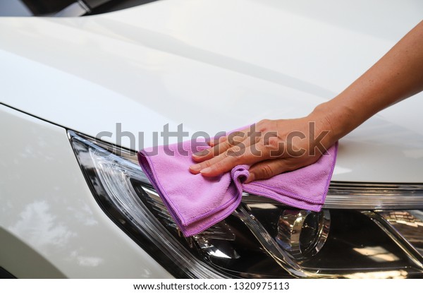 Closeup of\
headlight of white car cleaning, polishing by woman owner\'s hand\
with purple microfiber cloth in sunny\
day.