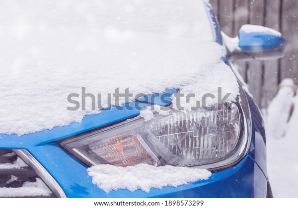 close-up of headlights of\
a blue car covered with snow. winter, snowfall, cold, frost.\
Horizontal photo.