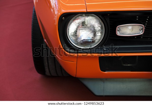 Closeup headlights of an orange\
retro car. Muzzle cars, bumper and the appearance of muscle\
car.