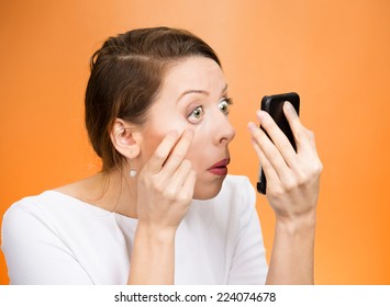 Closeup headshot funny looking woman pulling down eyelid checking her eye looking in morrow feels unwell isolated orange background. Human face expression. Health issues, problems concept