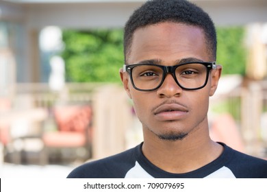 Closeup Headshot Portrait Of Fine Young Man With Big Glasses, Undergrad Student, Straight Face, Isolated On Outside Outdoors Background.