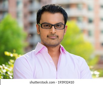 Closeup Headshot Portrait, Happy Handsome Businessman In Pink Shirt, Wearing Black Glasses Relaxing Outside Of His Office During Sunny Day, Isolated On A City Urban Background. Corporate Success