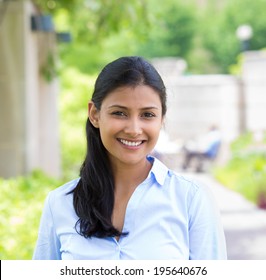 Closeup headshot portrait, young beautiful business woman in blue shirt smiling isolated on nature background with trees. Positive human emotion facial expression