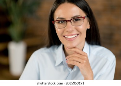 Close-up Headshot Of A Pretty, Smiling Brunette Caucasian Businesswoman, Small Business Owner, Company Leader Or Sales Manager, Successful Real Estate Agent, Looks At Camera, Stands In Office, Smiles