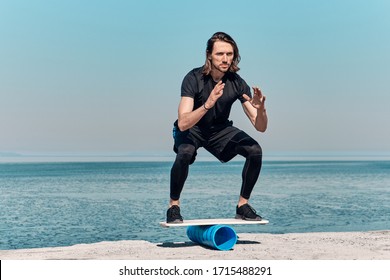 Closeup Of Healthy Handsome Active Man With Fit Muscular Body keeping balance on the wooden board against the background of sea on summer day