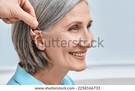 Close-up of hearing aid near senior female patient's ear at audiology clinic. Hearing solutions, hearing BTE aids