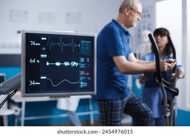 Close-up of heart rate monitor taking a pulse of senior patient during physical rehabilitation activity. Screen showing vital signs of elderly man while he uses stationary bicycle for physiotherapy. - Powered by Shutterstock