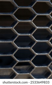 A close-up of a hexagonal metal grid pattern with a dark background.