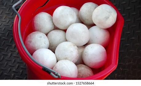 Close-up high angle view into a red plastic bucket full of white polo balls stored after a polo match
