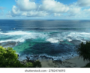 Close-up high angle view of powerful turquoise ocean waves crashing with white foam over a rocky coral reef shore.