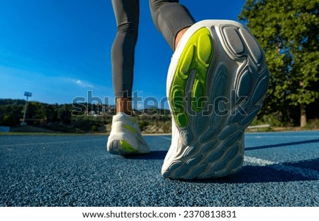 Close-up high angle view of the sole of a flexed running shoe of a female runner in running tights preparing to start a race on a blue running track. Sunny day under a clear blue sky.