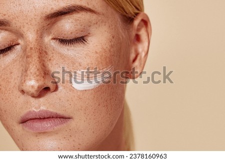 Close-up high detailed cropped shot of a young female with moisturizer on her cheek