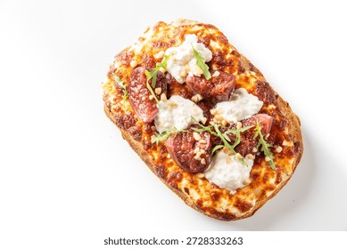 A close-up, high-angle shot of a delicious rectangular flatbread pizza topped with melted golden cheese, sweet sliced figs, creamy white ricotta or goat cheese, pine nuts, and fresh green arugula, on a white background