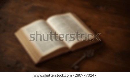 A close-up, high-angle view of an old, weathered open book lying on a rustic wooden surface next to a vintage key.