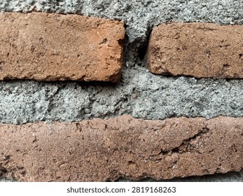 A close-up, high-angle view of a rustic brick wall showing the rough texture of red bricks held together by coarse, grey cement mortar.