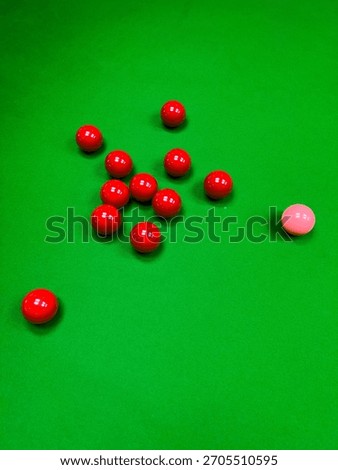 A close-up, high-angle view of several red snooker balls and one pink ball scattered on the bright green felt of a billiards table. The image has a shallow depth of field, focusing on the balls.