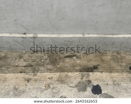 A close-up, high-angle view showcasing the rough and weathered textures of a concrete wall and ground. The image is divided horizontally into sections, revealing different shades and finishes of grey 
