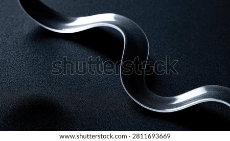 A close-up, high-angle view of a sleek, metallic ribbon with a polished surface, elegantly curving across a dark, subtly textured background.