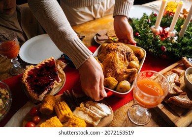 Close-up high-angle view of young man putting dish with roasted hot turkey on holiday dinner table served for Christmas family party, celebrating thanksgiving day with roasted turkey for dinner. - Powered by Shutterstock