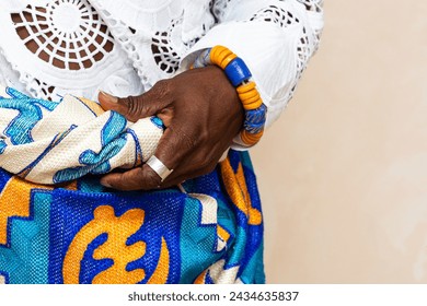 close-up highlights the hands of an African person clad in vibrant traditional attire, adorned with colorful beads and a woven bracelet, exemplifying the intricate beauty of African cultural garments - Powered by Shutterstock