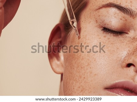 Close-up highly detailed shot of female skin with freckles and pipette with serum. Cropped shot of young woman with smooth perfect skin applying liquid serum on face.