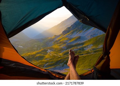 closeup hiker legs  lie in touristic tent on mountain valley background, view from touristic tent to early morning mountain valley