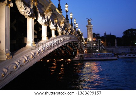 Closeup of the historical bridge on the river Seine in Paris by night with a boat bateau mouche floating over the water and  the statue of Place de la Concorde on background and the street lights on