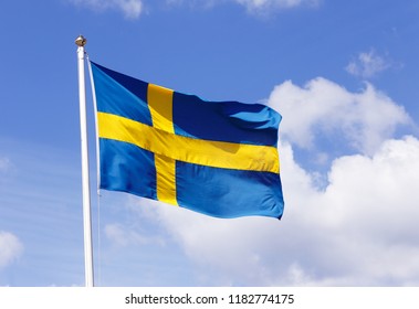 Close-up of a hoisted Swedish flag agiants a blue sky with clouds.