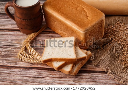 Close-up of homemade bread. Peasant square bread and wheat spikelets with space for text. Homemade baking. White bread with flour and milk on wooden chopping board wheat rye ears copy space.