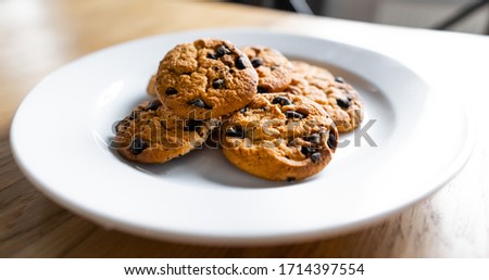 Close-up of homemade chocolate chip cookies. Basic drop cookies with chocolate morsels. Choc chip cookies in a white plate on a wooden table. Traditional handmade chewy cookies with chocolate chunk