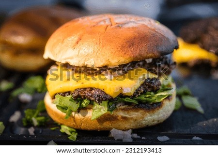 
close-up of homemade double smash burger with cheese, lettuce, onion and dressing lying on a cutting board