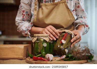 Close-up of homemade pickled canned cucumbers and chili peppers in sterilized glass jars in the hands of a young woman housewife. Fresh fragrant ingredients and culinary herbs on a kitchen table - Shutterstock ID 2189245817