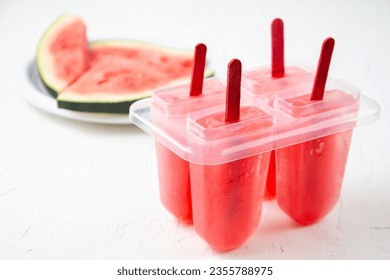 Close-up of homemade watermelon popsicles in mold on white table with watermelon slices, selective focus, horizontal, with copy space - Powered by Shutterstock