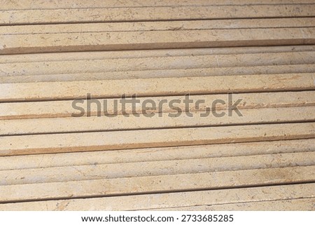 Close-up of horizontal light-brown rectangular planks with parallel grooves and a slightly rough, sandy texture.
