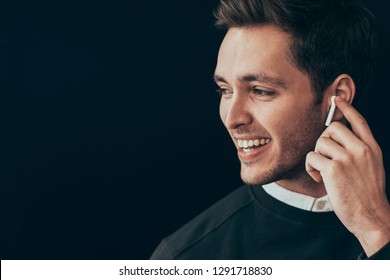 Closeup horizontal portrait of young handsome man smiling and have a call with a colleague isolated on black background holding wireless earphone with finger. Businessman using wireless headphone. - Powered by Shutterstock