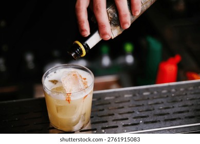 Close-up Horizontal Shot of a Bartender Adding Aromatic Bitters to the Foam of a Fresh Sour Cocktail in a Rocks Glass