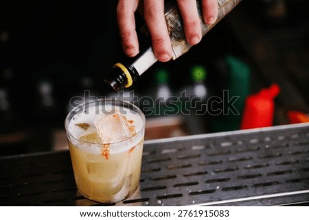 Close-up Horizontal Shot of a Bartender Adding Aromatic Bitters to the Foam of a Fresh Sour Cocktail in a Rocks Glass