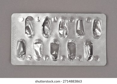 A close-up, horizontal shot of an empty silver blister pack that once held ten pills, placed on a gray background