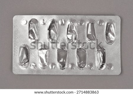 A close-up, horizontal shot of an empty silver blister pack that once held ten pills, placed on a gray background