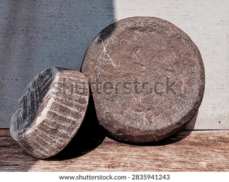 A close-up horizontal shot of two rustic round stone millstones placed side by side on a wooden surface with dramatic sunlight casting strong diagonal shadows.