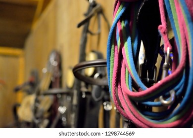 Closeup Of Horse Tackle ‘tack’ In A Stable. Head Collars, Lead Ropes And Bridles Hang On A Wooden Stable Wall.