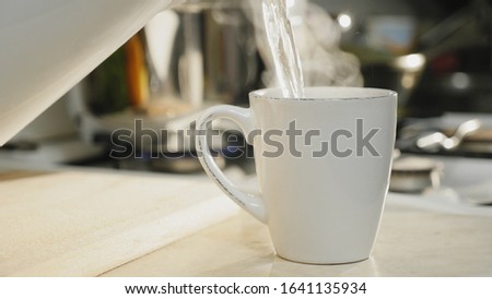 Close-up of hot boiled water is poured into a white ceramic cup on the table in the kitchen, brewing morning coffee