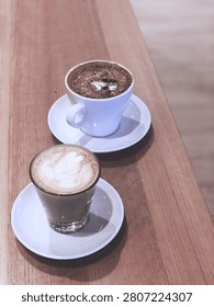 A close-up of hot drinks featuring a flat white and a cappuccino served together on a café table. The image highlights rich crema, warm tones, and a cozy café atmosphere, ideal for coffee culture and lifestyle themes.