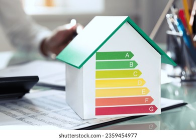 Close-up Of House Model Showing Energy Efficiency Rate In Front Of Businessperson's Hand Using Calculator - Powered by Shutterstock