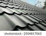 Close-up house roof with steel roofing sheet. Traditional metal shingle tiles. Gray modular tile effect roof panel. Profiled metallic corrugated pantile as clay or concrete slate. Building