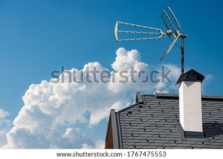 Closeup of a house roof with a television aerial, on a clear blue sky with clouds and copy space