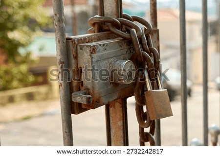 Close-up of house security with an rusty gate lock and old chain with closed padlock on iron gate close-up. Protection, urban insecurity, and privacy.