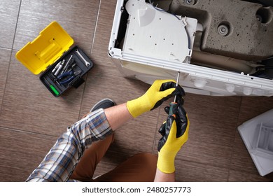 Close-up of a household appliance repairman disassembling a washing machine with a screwdriver. Professional repair of household appliances. - Powered by Shutterstock