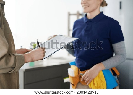 Close-up of housewife signing a contract with cleaning service worker to hire professional to do housework